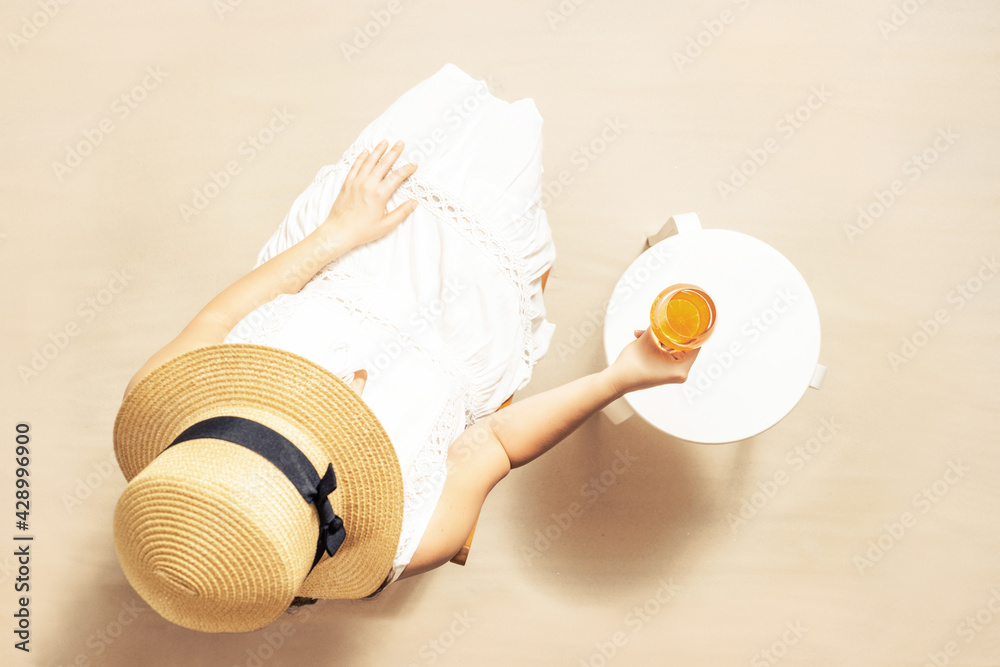 Alone woman sitting with glass of juice with piece orange on the table. Female relaxation on the sandy beach at summer vacation. Top view