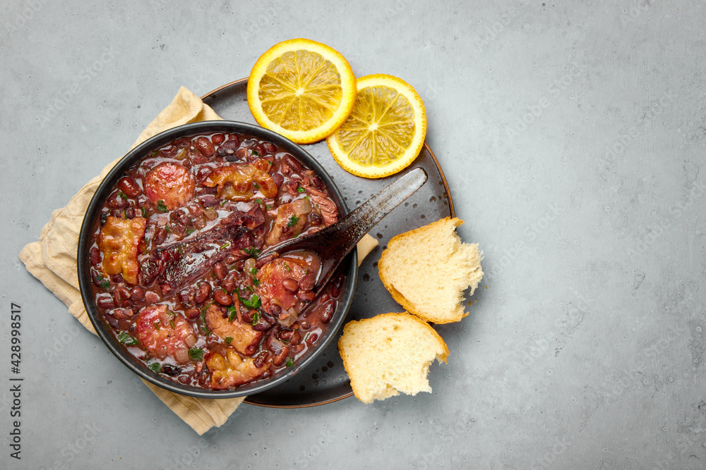Feijoada in black bowl gray concrete table top. Brazilian and portuguese cuisines traditional beans meat stew Feijoada in black bowl gray concrete table top. Brazilian and portuguese cuisines traditional beans meat stew