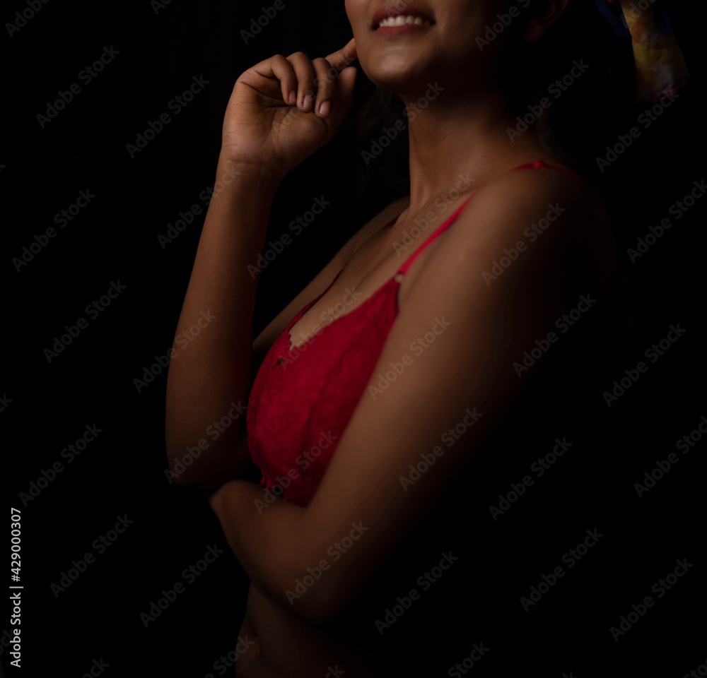 Naklejka premium Portrait of an young and attractive Bengali Indian brunette girl wearing red lingerie posing in front of a black studio background. Indian lifestyle and boudoir photography.