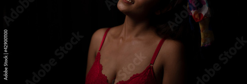 Portrait of an young and attractive Bengali Indian brunette girl wearing red lingerie posing in front of a black studio background. Indian lifestyle and boudoir photography.