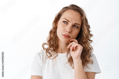 Serious thoughtful woman making hard decision, looking aside at upper left corner, thinking and frowning, standing over white background