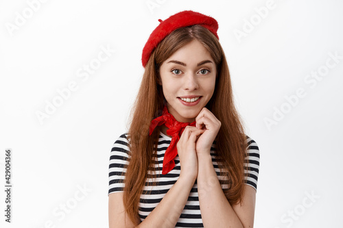 Close up of cute female student in french hat clothes, smiling and looking cute at camera, standing against white background