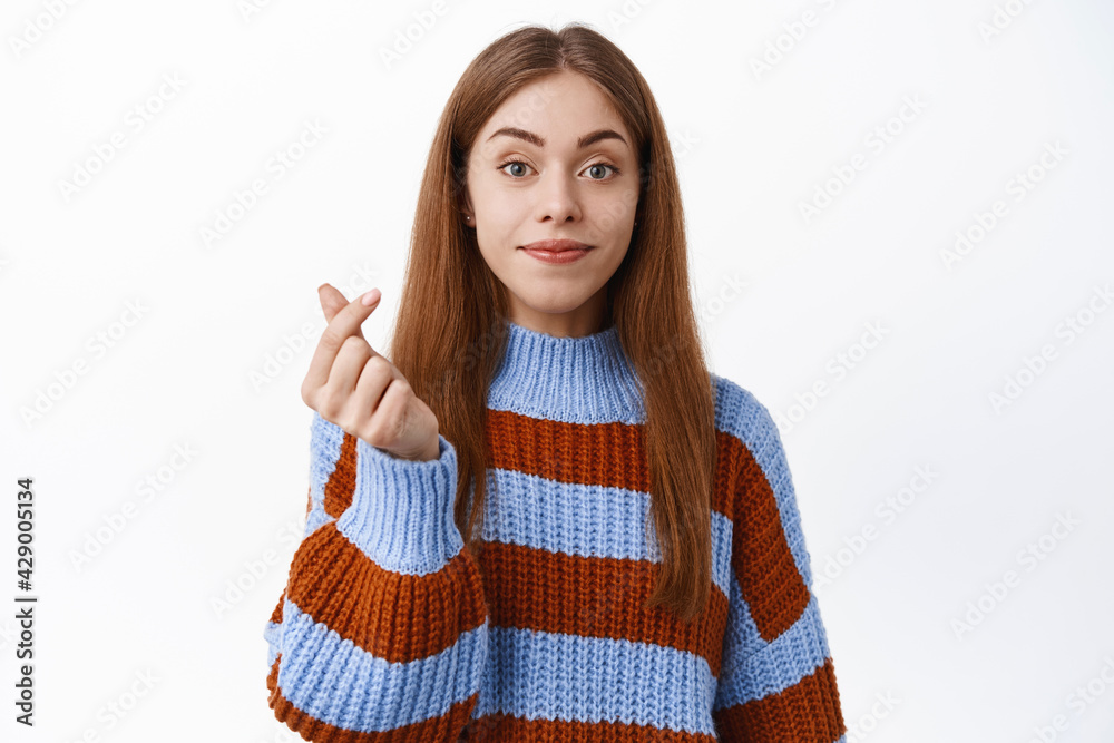 Attractive caucasian woman in sweater, showing finger heart sign and smiling, express like or love, standing over white background