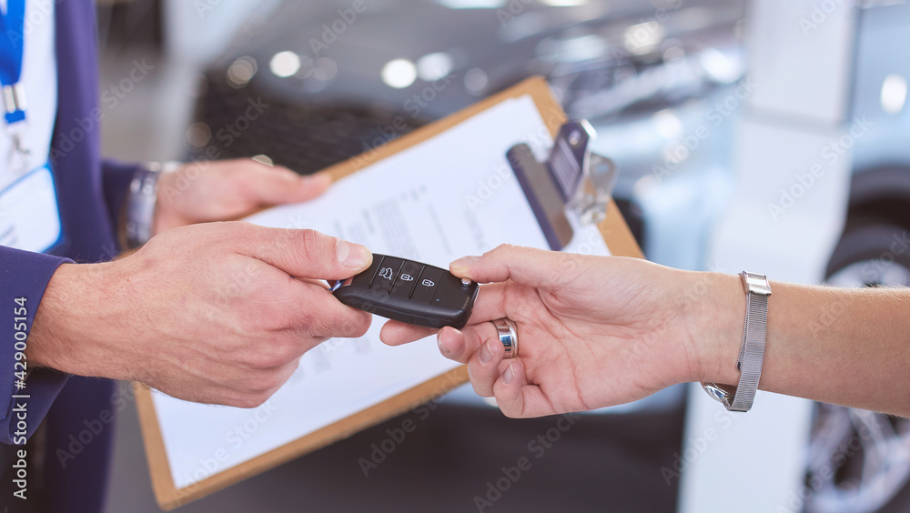 Car salesman sells a car to happy customer in car dealership and hands over the keys