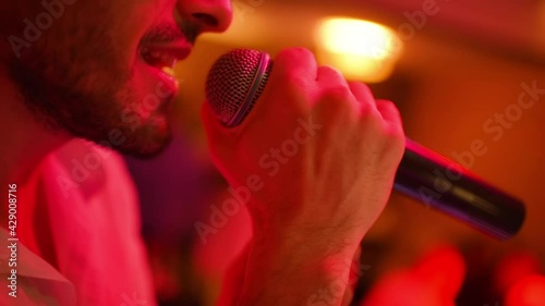 a bearded male singer sings into a microphone at karaoke or in a nightclub.
