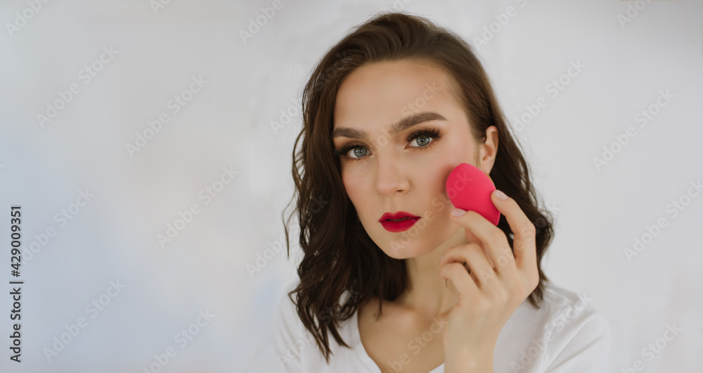 Portrait of beautiful young woman is having fun with pink egg sponge. Isolated over white background. Copy space. Skin care and beauty concept. Banner for website Portrait of beautiful young woman is having fun with pink egg sponge. Isolated over white background. Copy space. Skin care and beauty concept. Banner for website