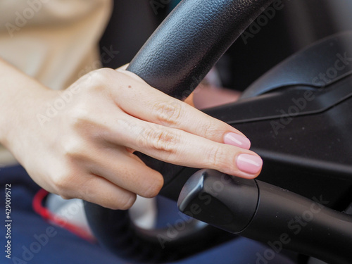 Focus on the hand of a woman driving at close range is pressing the car's turn signal.