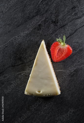 triangular cake with white cream on top and half juicy strawberries on a gray stone background