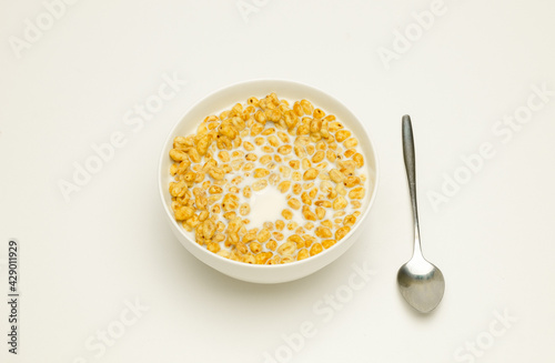 wheat flakes with milk in a white cup and tablespoon on a white background