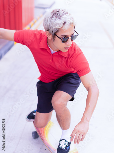 Asian handsome man surfing skateboard and abbreviate on skate board at skateboard street way in daylight time, summer holiday