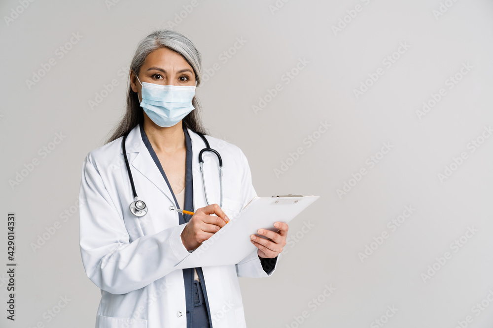 Asian mature woman in medical uniform and mask holding notepad