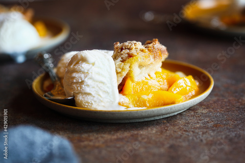 Freshly baked drop biscuit peach cobbler served with French vanilla ice cream over a dark rustic background.