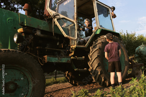 The boys are playing and looking at a large farm tractor.