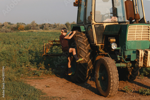 The boys are playing and looking at a large farm tractor.