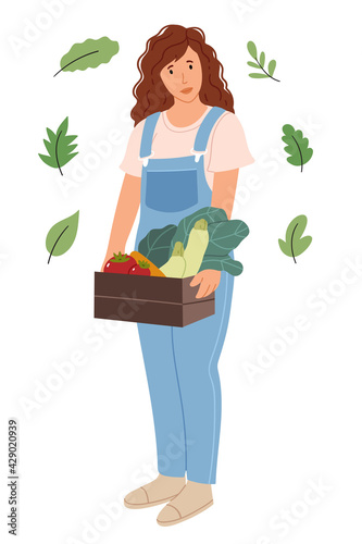 Girl farmer holding a box of vegetables.A woman in denim overalls holds a zucchini, tomato, mortar. Work in the garden and orchard.