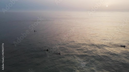 Aerial view of people doing surf in Atlantic Ocean open water at sunset along Caparica coastline, Lisbon, Portugal.