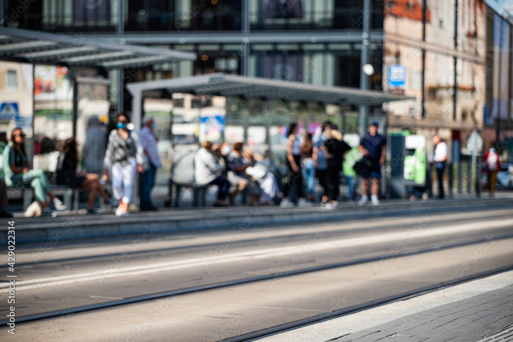 Lots of people waiting at the tram, bus stop in the city center, blurry photo 