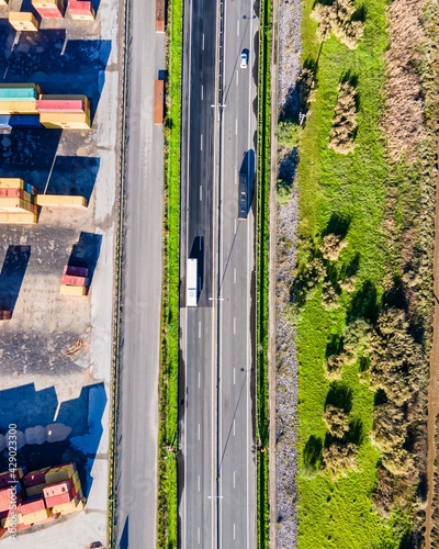 Lisbon, Portugal - 05 December 2020: Aerial view of a few vehicles driving on an empty highway road next a container ships warehouse, Lisbon, Portugal.