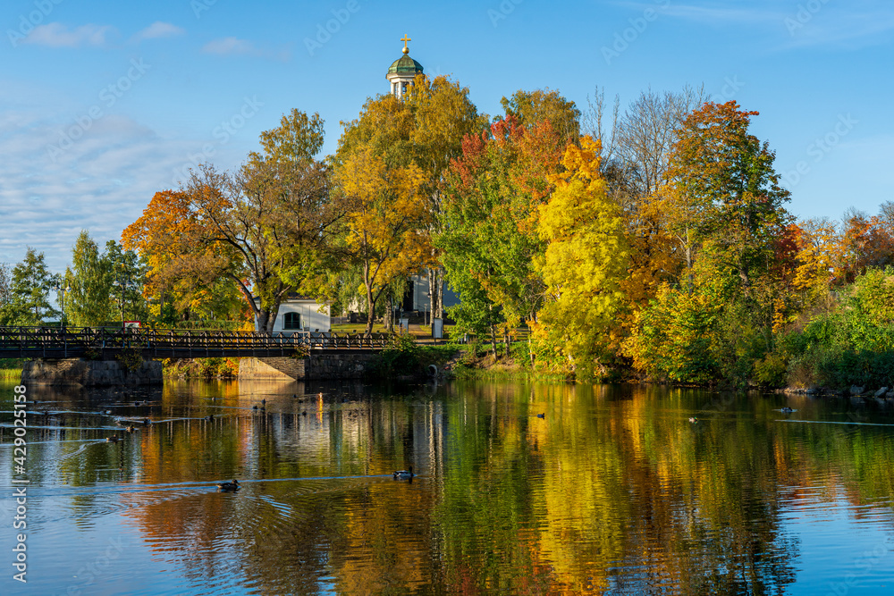 Church tower by a river surrounded by vibrant autumn colored trees