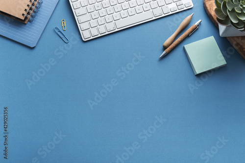 Blue desk with keyboard blank note, supplies. Stylish home office workspace. Overhead view.
