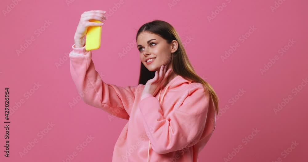 Beautiful woman takes a selfie on the phone and posing, pink background studio Beautiful woman takes a selfie on the phone and posing, pink background studio