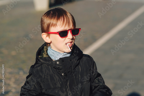 Boy with lollipop. Preteen boy having fun outdoors. Boy wearing trendy sunglasses. Urban street style.