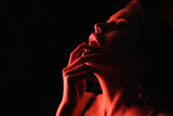red lighting on sexy woman touching lips isolated on black.