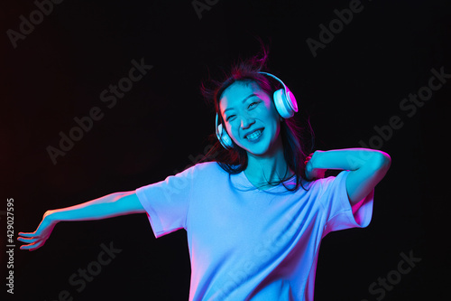 Asian young woman's portrait on dark studio background in neon. Concept of human emotions, facial expression, youth, sales, ad. © master1305