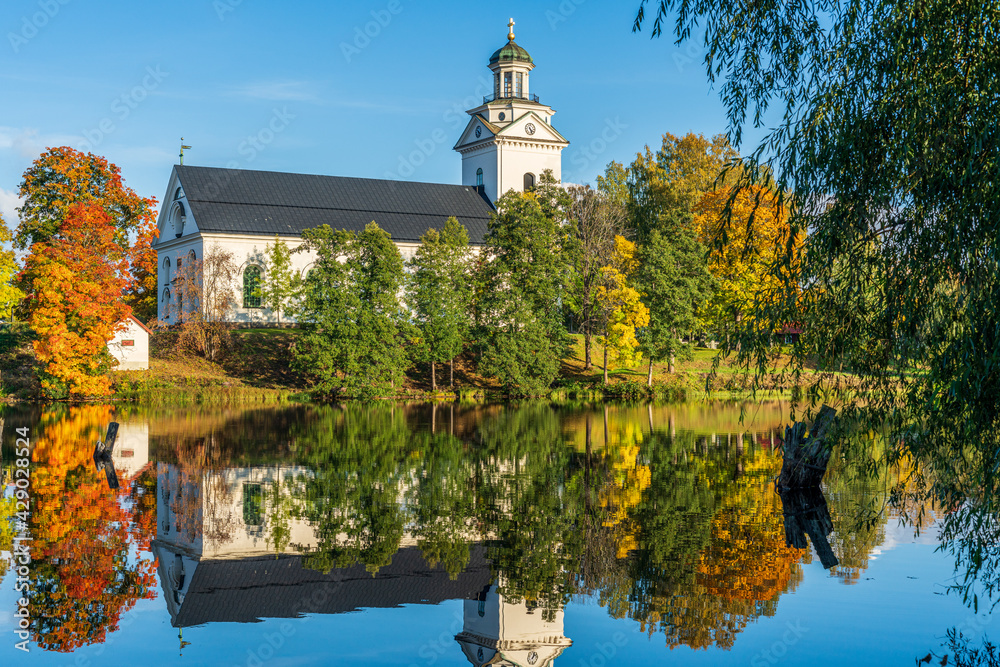 Fototapeta premium White church by a river in Sweden surrounded by autumn colored trees