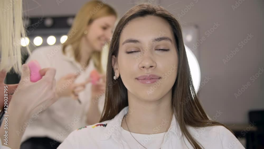 Make-up specialist improving model's appearance. Close-up of a smiling woman sitting in a studio while preparing for a photoshoot. High quality 4k footage Make-up specialist improving model's appearance. Close-up of a smiling woman sitting in a studio while preparing for a photoshoot. High quality 4k footage