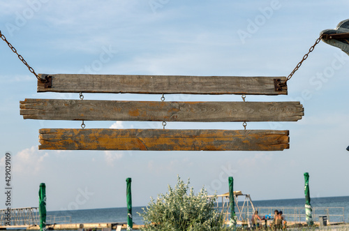 Vintage wooden plank signs on the chains near the beach bar. Old wood signboard with metal chain and three planks at coast.