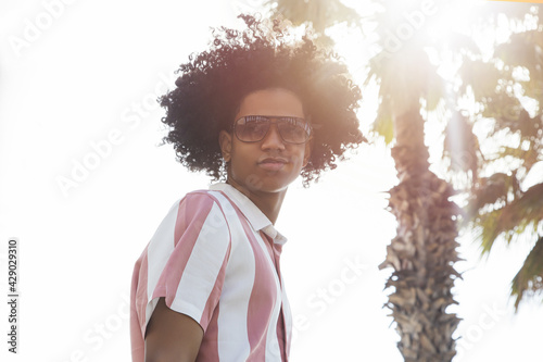 Portrait of a cool looking young African man with a palm tree and sunlight in the background