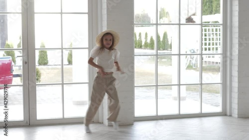 Close up of active female child girl with golden hair, wearing white elegant costume, dancing dance at home, moving cheerful, waving her arms in different directions, performing movement on camera photo