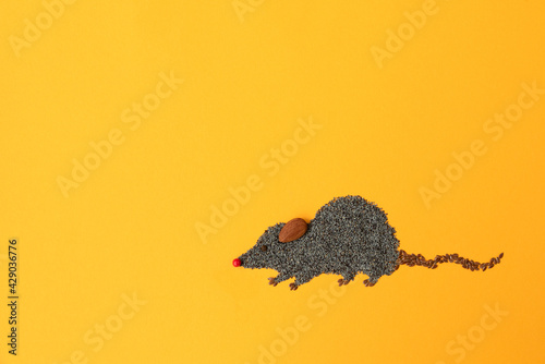 Cute mouse made of flax and poppy seeds on yellow background. Food art creative concept