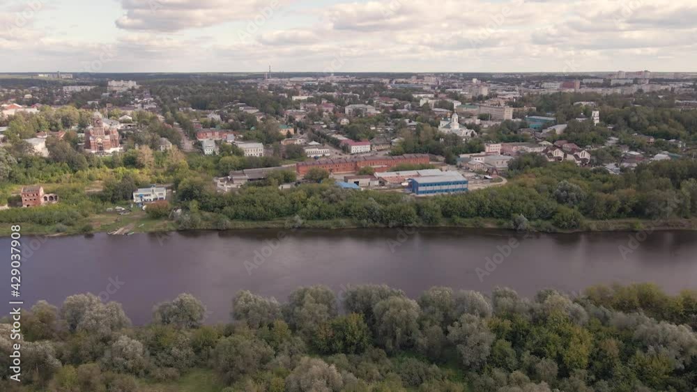 Fly over wooded areas, a wide river and cities in the distance. The outskirts of the city on the river bank are surrounded by dense greenery with thick white clouds against a blue sky. Fly over wooded areas, a wide river and cities in the distance. The outskirts of the city on the river bank are surrounded by dense greenery with thick white clouds against a blue sky.