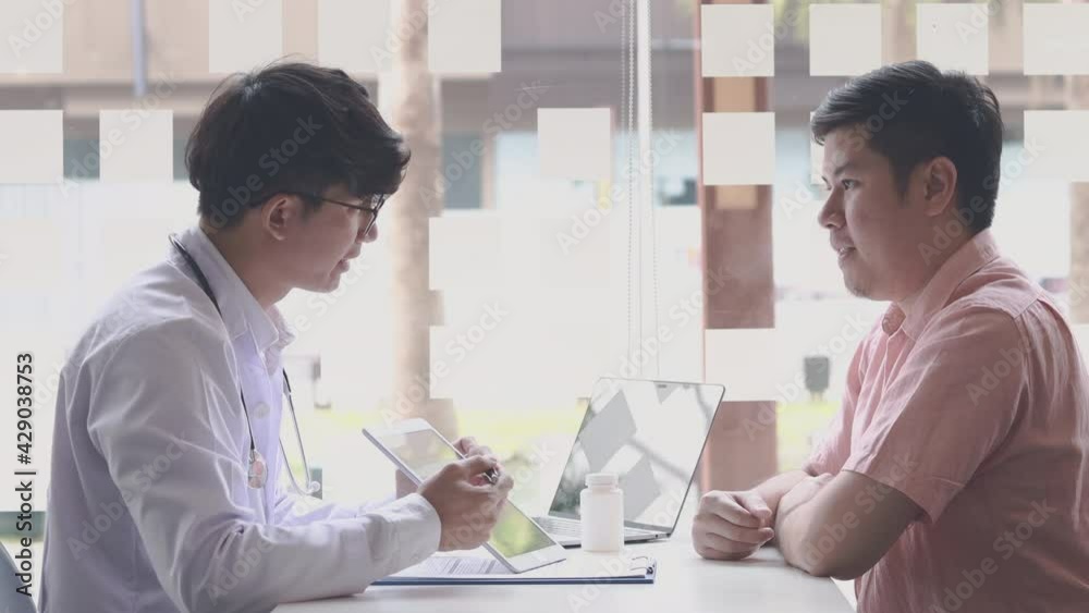 Young Asian man in a white robe talks to a man, Doctors diagnose diseases and give advice or treatment solutions to patients in the hospital examination room, Explaining medical examination results.