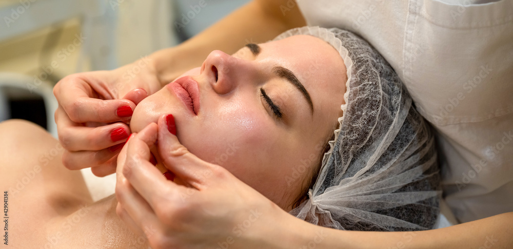 Fototapeta premium Beautiful young woman getting a face massage treatment at beauty salon. Fingers of masseur. Facial skin care. Woman at beauty spa salon.