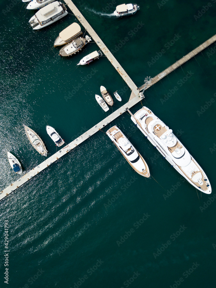 Aerial top down view of boat dock and yacht port in Budva, Montenegro. White private motor boats are moored to pier on Adriatic sea coast. Yacht club boats parking. Photo from drone. Minimalism.
