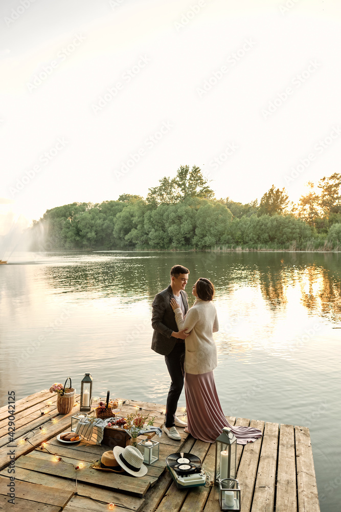 A loving couple arranged a romantic date on the banks of the river. A young man hugs a girl in an elegant dress. Vertical orientation.