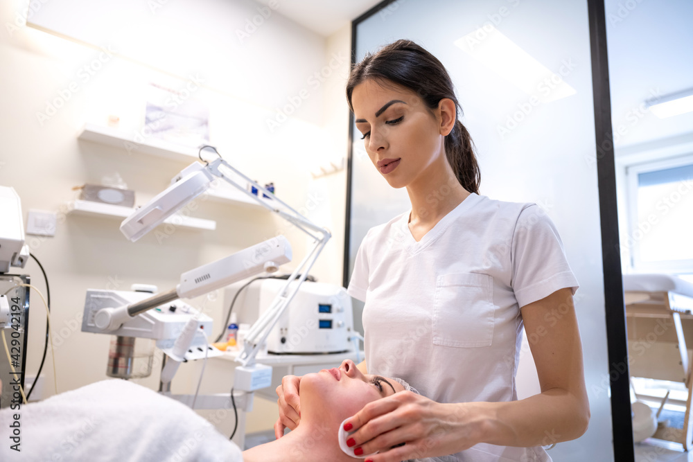 Young woman relaxing during cosmetic procedure in cosmetology salon. Female beautician wiping skin with cotton disks. Concept of skin care. Young woman relaxing during cosmetic procedure in cosmetology salon. Female beautician wiping skin with cotton disks. Concept of skin care.