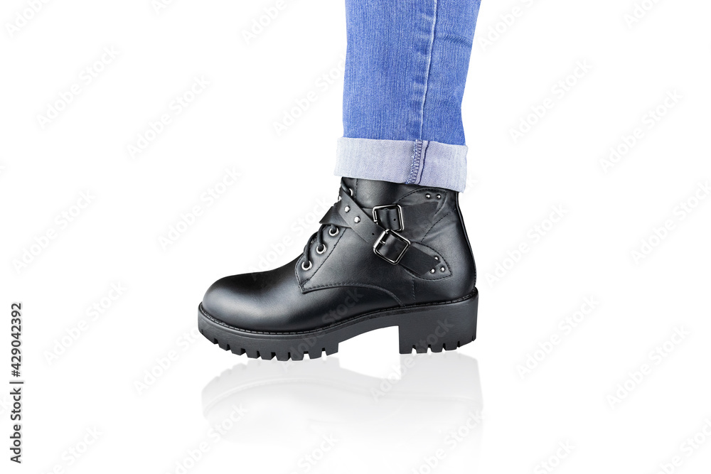Leg in blue rolled up jeans and black lace-up boot with buckles and straps, isolated on white. Leg in blue rolled up jeans and black lace-up boot with buckles and straps, isolated on white.