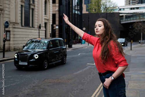 Young woman in red shirt hailing a taxi in urban London.