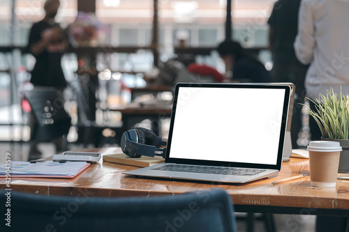  Laptop computer with supplies on wooden table with blurred group of people background.