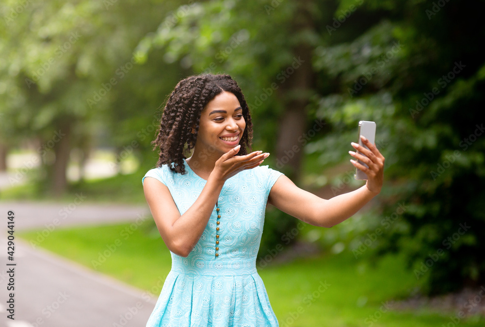 Happy black girl talking to her boyfriend online, sending air kiss on mobile phone at park Happy black girl talking to her boyfriend online, sending air kiss on mobile phone at park