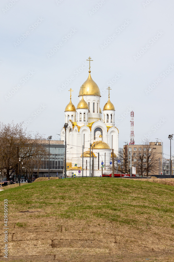 Cityscape with green grass loan, street, buildings, Golden shining domes of white church in blue sky with clouds in Ivanovo, Russia