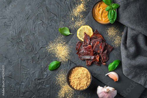 Obraz na płótnie Beef jerky with mustard, garlic and basil on a black background.