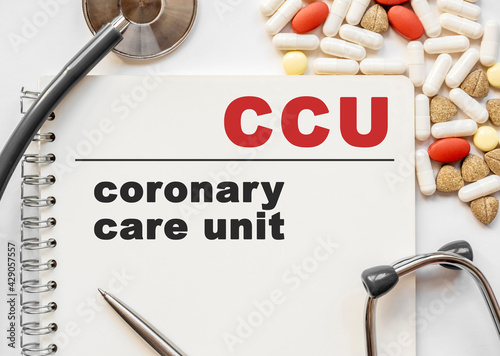 Page in notebook with coronary care unit CCU on white background with stethoscope and group of pill. Medical concept. Term and abbreviation photo