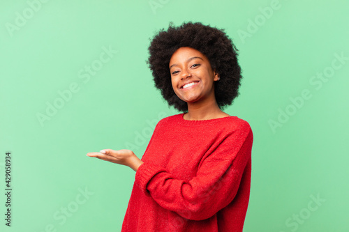 afro black woman smiling cheerfully, feeling happy and showing a concept in copy space with palm of hand