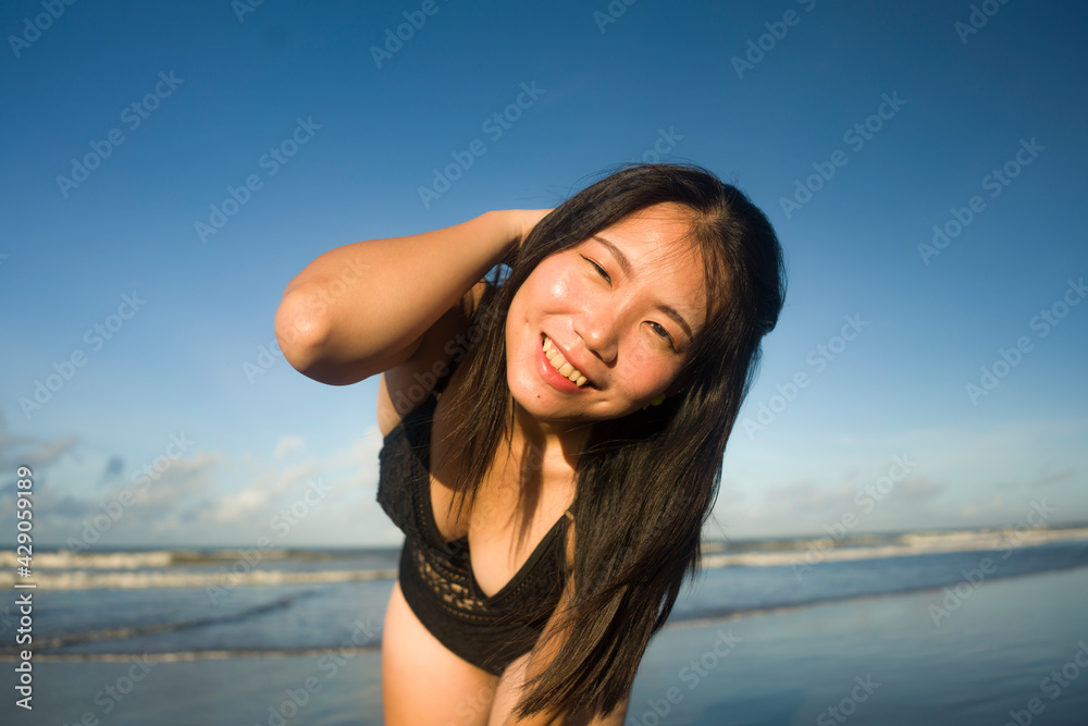 Summer lifestyle portrait of young happy and attractive Asian Chinese woman in bikini at beautiful beach enjoying holiday trip to tropical island