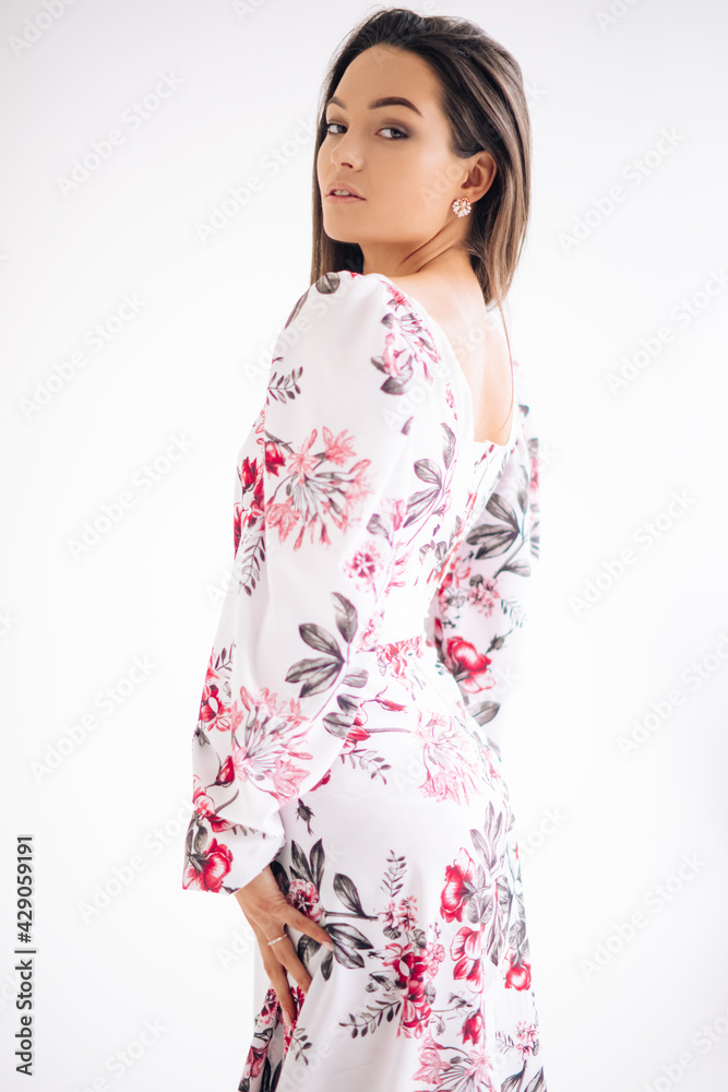Young woman stands dressed in floral pattern dress on white background. Young woman stands dressed in floral pattern dress on white background.